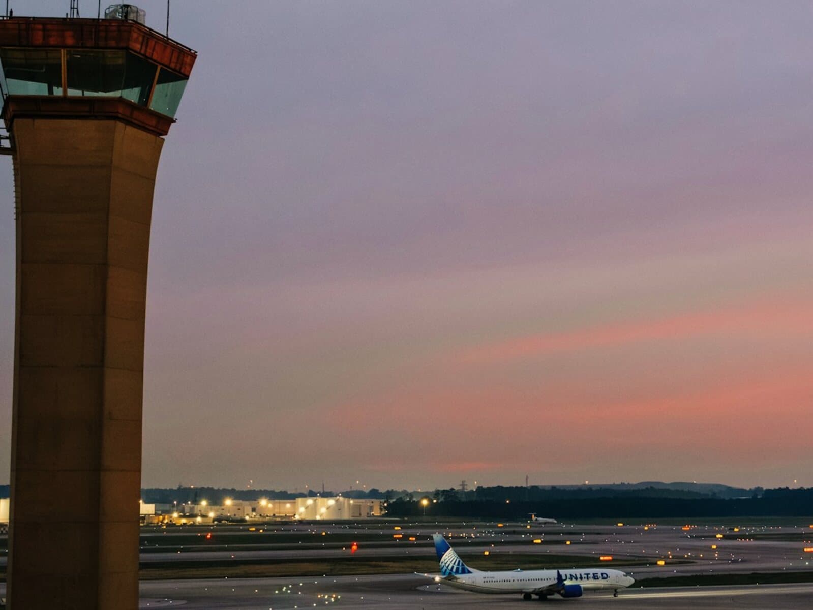 The control tower at George Bush Intercontinental Airport at dusk, with a jet taxiing